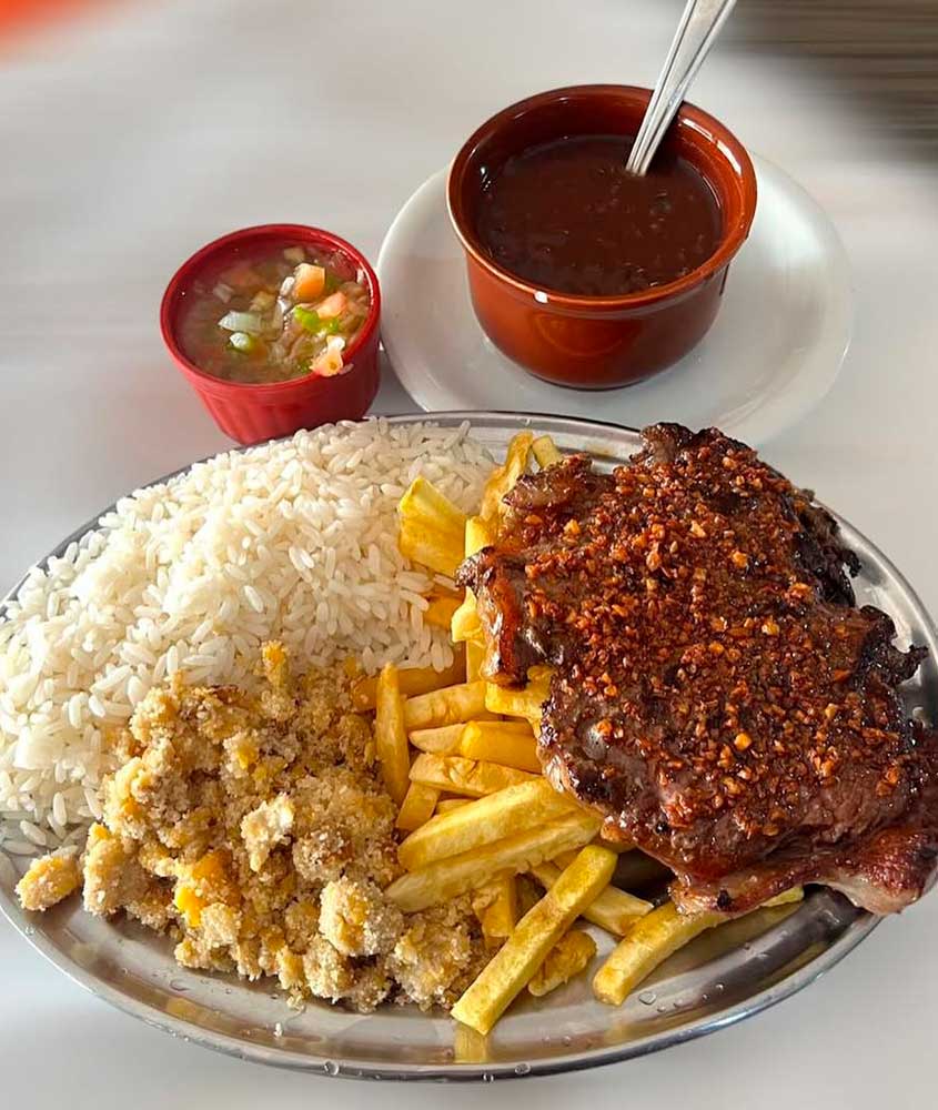 Prato feito com bife acebolado, arroz branco, farofa, batata frita, acompanhado de feijão e vinagrete.
