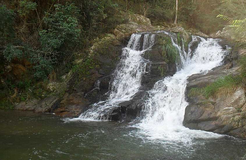 Cachoeira de pequeno porte com queda d’água sobre pedras e vegetação ao redor, localizada na Reserva Biológica do Tinguá, Rio de Janeiro.