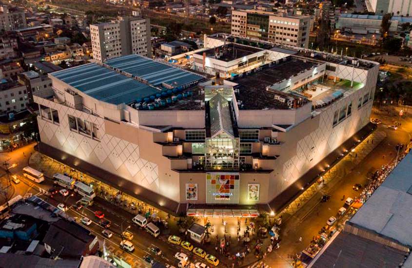 Vista aérea do Shopping de Madureira iluminado à noite, com fachadas modernas, movimento de pessoas e carros nas ruas ao redor.