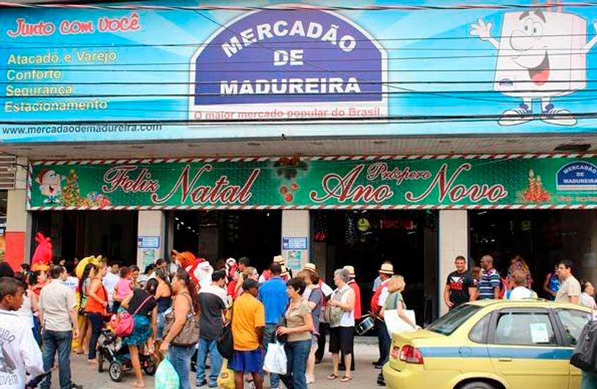 Fachada do Mercadão de Madureira decorada para o Natal e Ano Novo, com movimento intenso de pessoas e comércio popular.