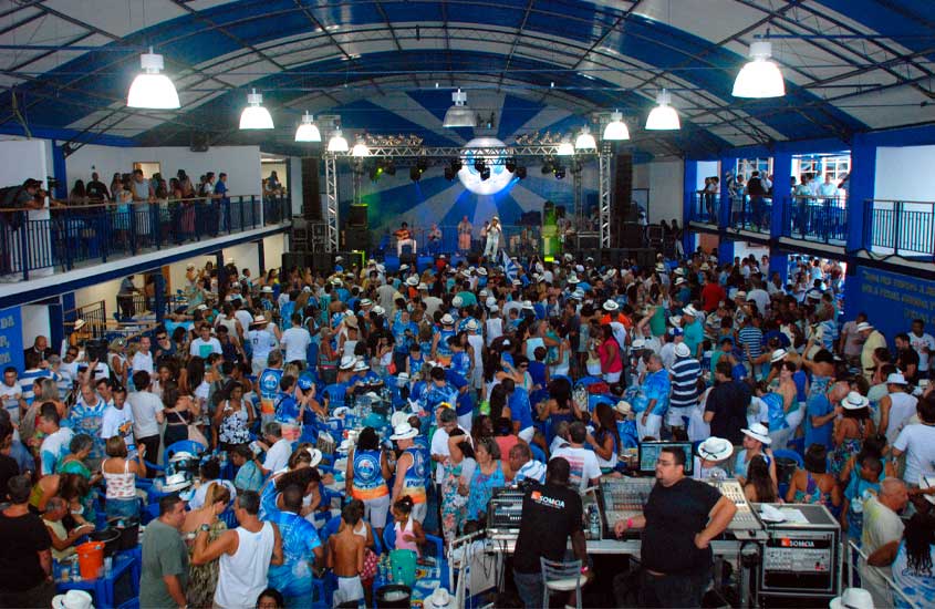 Quadra da Portela lotada durante um evento de samba, com palco iluminado ao fundo, músicos se apresentando e o público vestido em azul e branco acompanhando a festa.