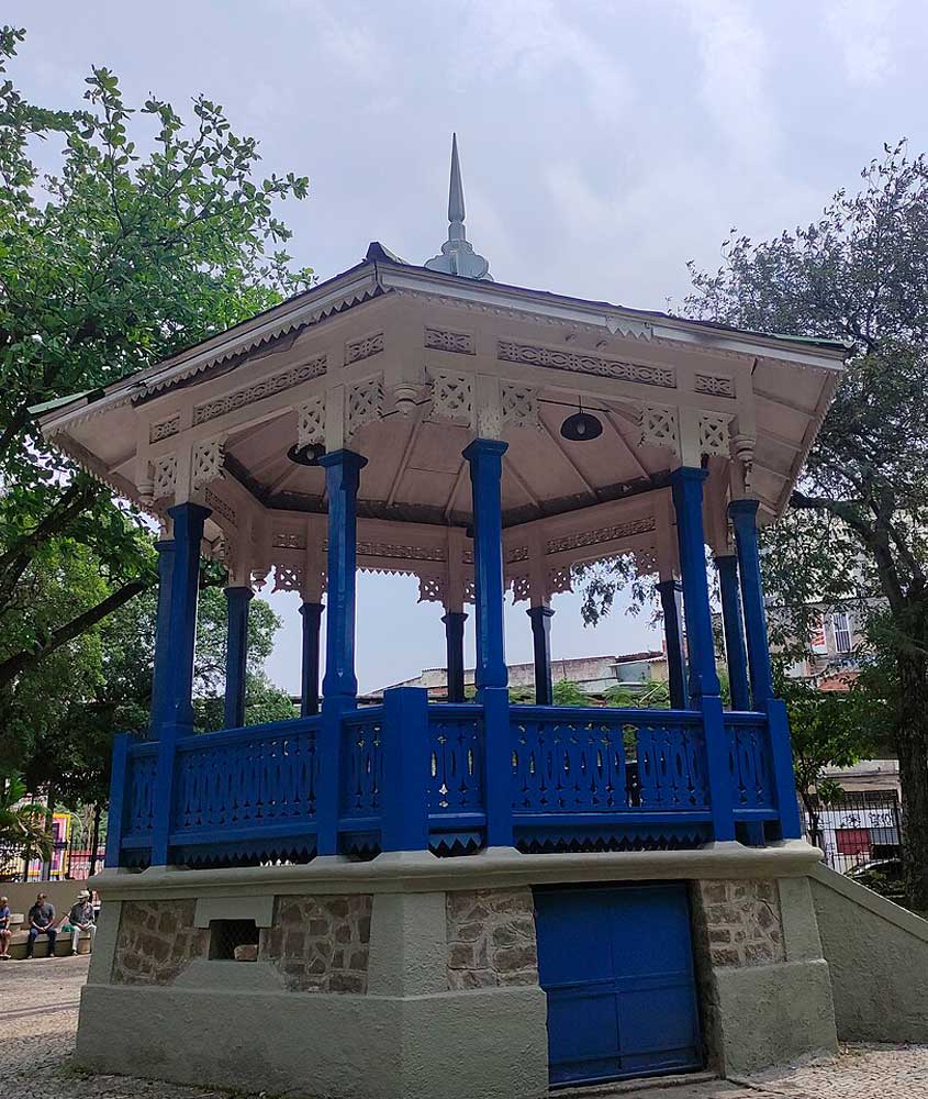 Coreto da Praça Agripino Grieco, no Méier, Rio de Janeiro, com estrutura azul e branca em estilo clássico, rodeado por árvores.