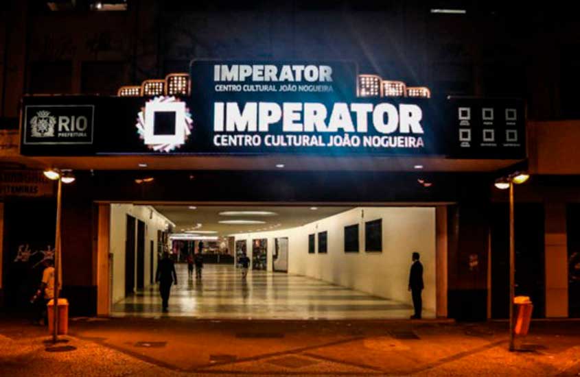 Entrada iluminada do Imperator – Centro Cultural João Nogueira, no Méier, com letreiro em destaque e pessoas passando pelo hall interno à noite.