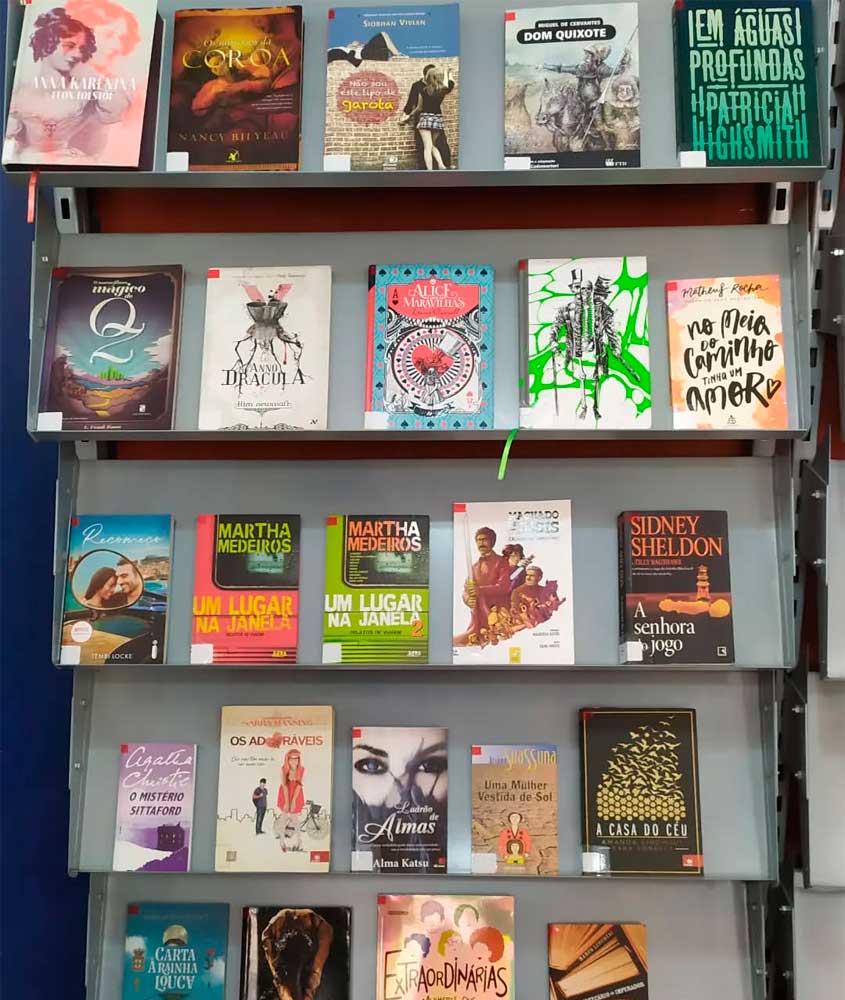 Estante de livraria ou biblioteca com diversos livros expostos de frente, entre eles títulos de autores como Agatha Christie, Martha Medeiros, Miguel de Cervantes e Sidney Sheldon.