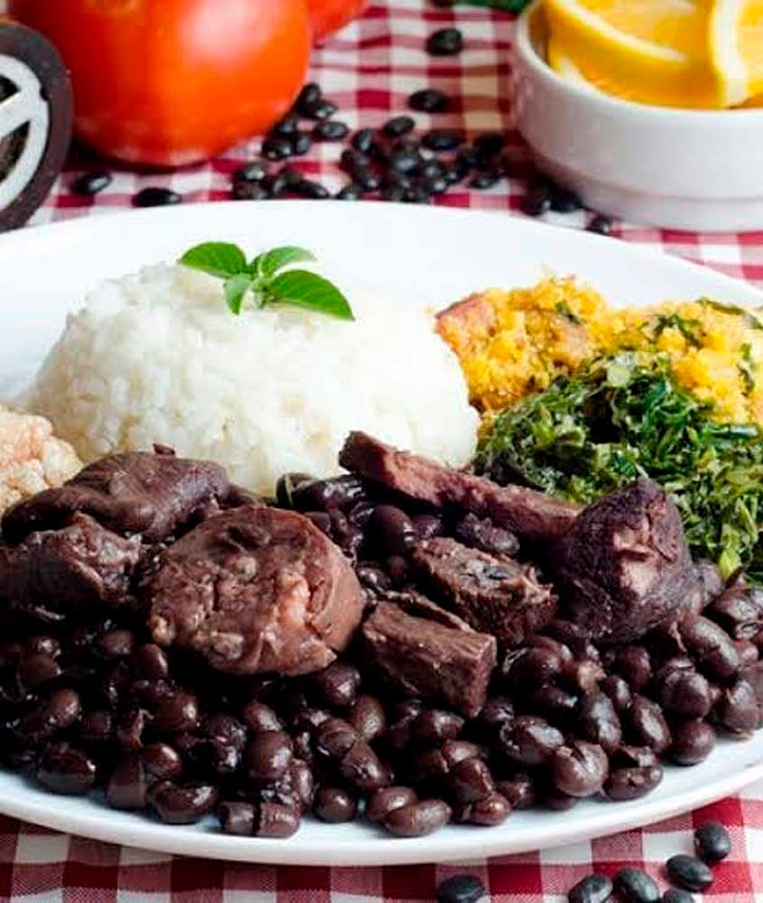 Prato de feijoada completa servido com arroz, couve refogada, farofa e torresmo, acompanhado de laranja fatiada.
