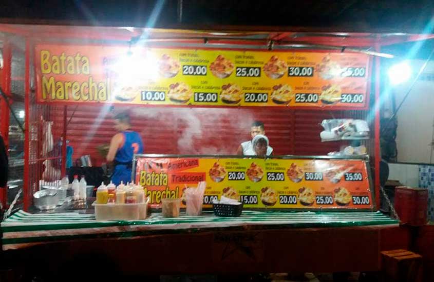 Barraca de rua Batata Marechal, com cardápio de batatas fritas servidas com diversos acompanhamentos. A fachada exibe placas com preços entre R$10 e R$35. Há garrafas de molhos e utensílios à frente do balcão, enquanto funcionários preparam os pedidos no interior.