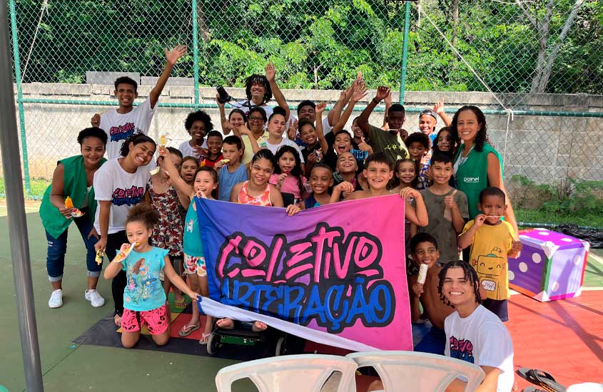 Grupo de crianças e jovens posando sorridentes ao lado de educadores, segurando uma faixa colorida com o nome “Coletivo ArterAção”.