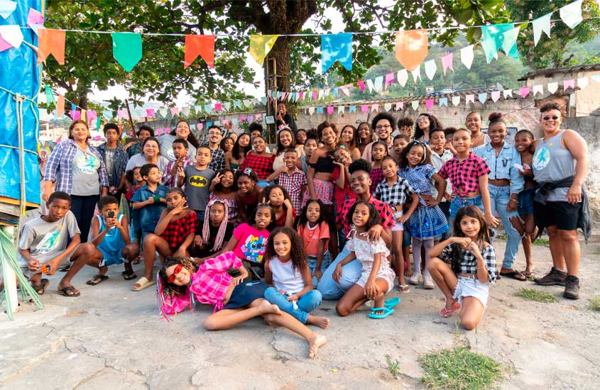 Crianças, jovens e adultos posam juntos em frente a bandeirinhas coloridas de festa junina, sorrindo e celebrando em clima de confraternização.